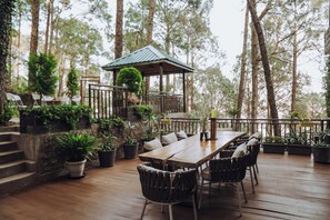 Een houten terras met een eettafel en stoelen, omringd door potplanten en een pergola.