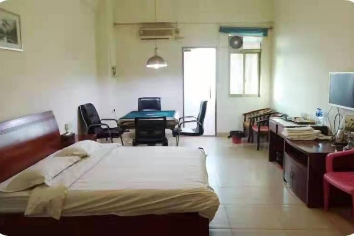 A hotel room with a bed, desk, chairs, a television, and a window.