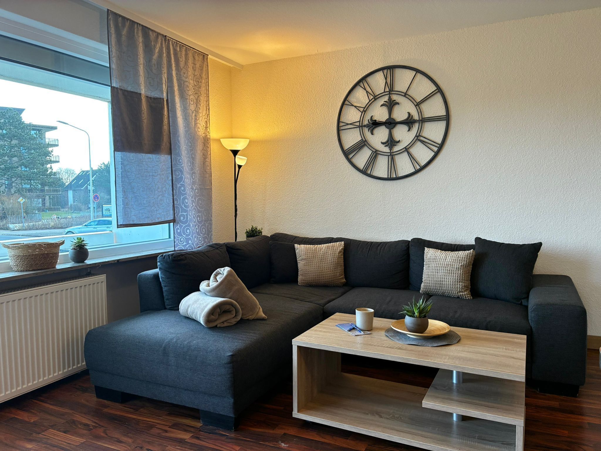 Uma sala de estar moderna com um sofá seccional, uma mesa de centro, um relógio de parede e uma janela com cortinas.