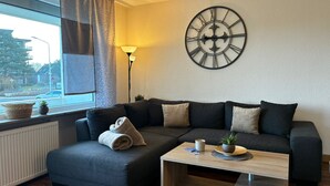 Un salon moderne avec un canapé d’angle, une table basse, une horloge murale et une fenêtre avec des rideaux.