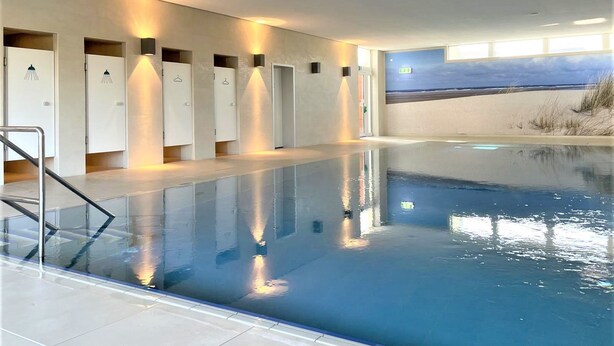 Une piscine offrant une vue dégagée sur la plage, un espace vestiaire et une barrière en verre.