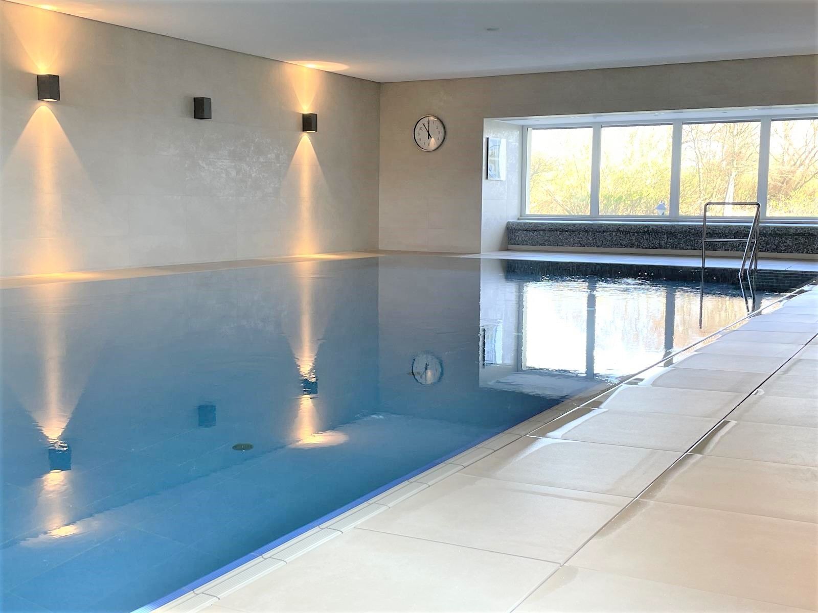 Une piscine intérieure offrant une vue dégagée sur l’eau, une horloge au mur et une fenêtre laissant entrer la lumière naturelle.
