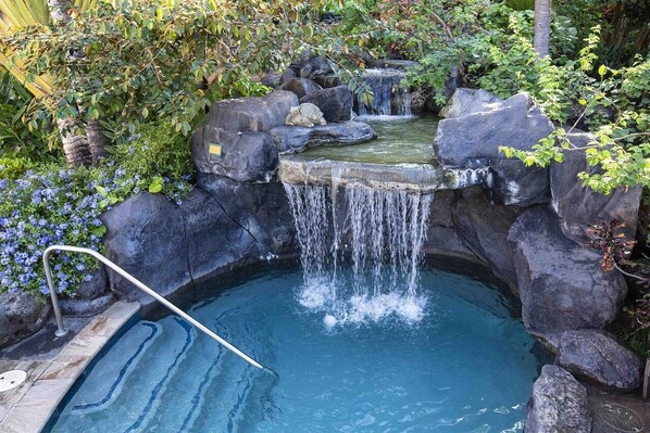 A small, naturalistic water feature with a cascading waterfall, surrounded by rocks and foliage.
