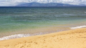 Une plage à l’eau claire, avec une montagne en arrière-plan.