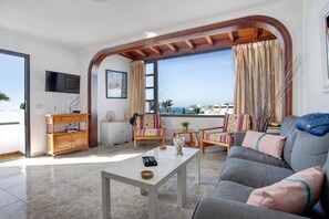 Un salón con sofá, sillas, mesa de centro, televisor y vista al mar.