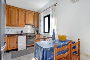 Una cocina compacta con armarios de madera, lavavajillas, horno y mesa de comedor con mantel azul.