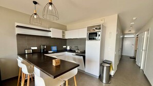 A modern kitchen with a central island, white chairs, and pendant lighting. - Apartment 2-6 pers, 2 bdr, balcony, pool, beach access, parking (La Tranche-sur-Mer)