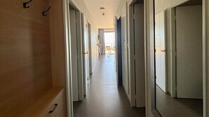 A hallway with doors leading to rooms, a wooden panel on the left, and a view into a balcony area. - Seafront Apartment, Direct Beach Access, Balcony, Pool, Jacuzzi, Parking, Sleeps 6 (La Tranche-sur-Mer)