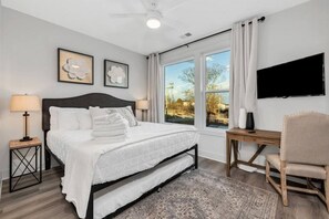 A bedroom with a bed, bedside lamps, a desk, a chair, a TV, and artwork on the wall.