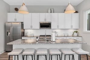 A modern kitchen with white cabinets, a stainless steel refrigerator, a built-in oven, and a granite countertop. - Tim & Faith's Rooftop - Brand New Nashville Hang Out (Nashville)