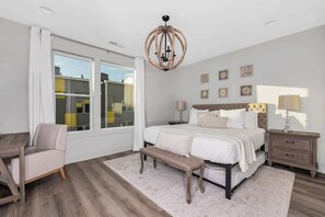 A bedroom with a large bed, a bench, a nightstand, and a chandelier.