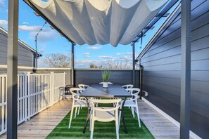 An outdoor patio with a table and chairs, a white fence, and a view of the sky.