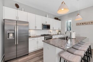 A modern kitchen with stainless steel appliances, white cabinetry, a granite countertop, and bar stools. - Tim & Faith's Rooftop - Brand New Nashville Hang Out (Nashville)