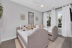 A bedroom with two beds, a ceiling fan, a large window with curtains, and artwork on the walls. - Tim & Faith's Rooftop - Brand New Nashville Hang Out (Nashville)