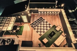 A rooftop terrace with a checkered floor, seating areas, and string lights.