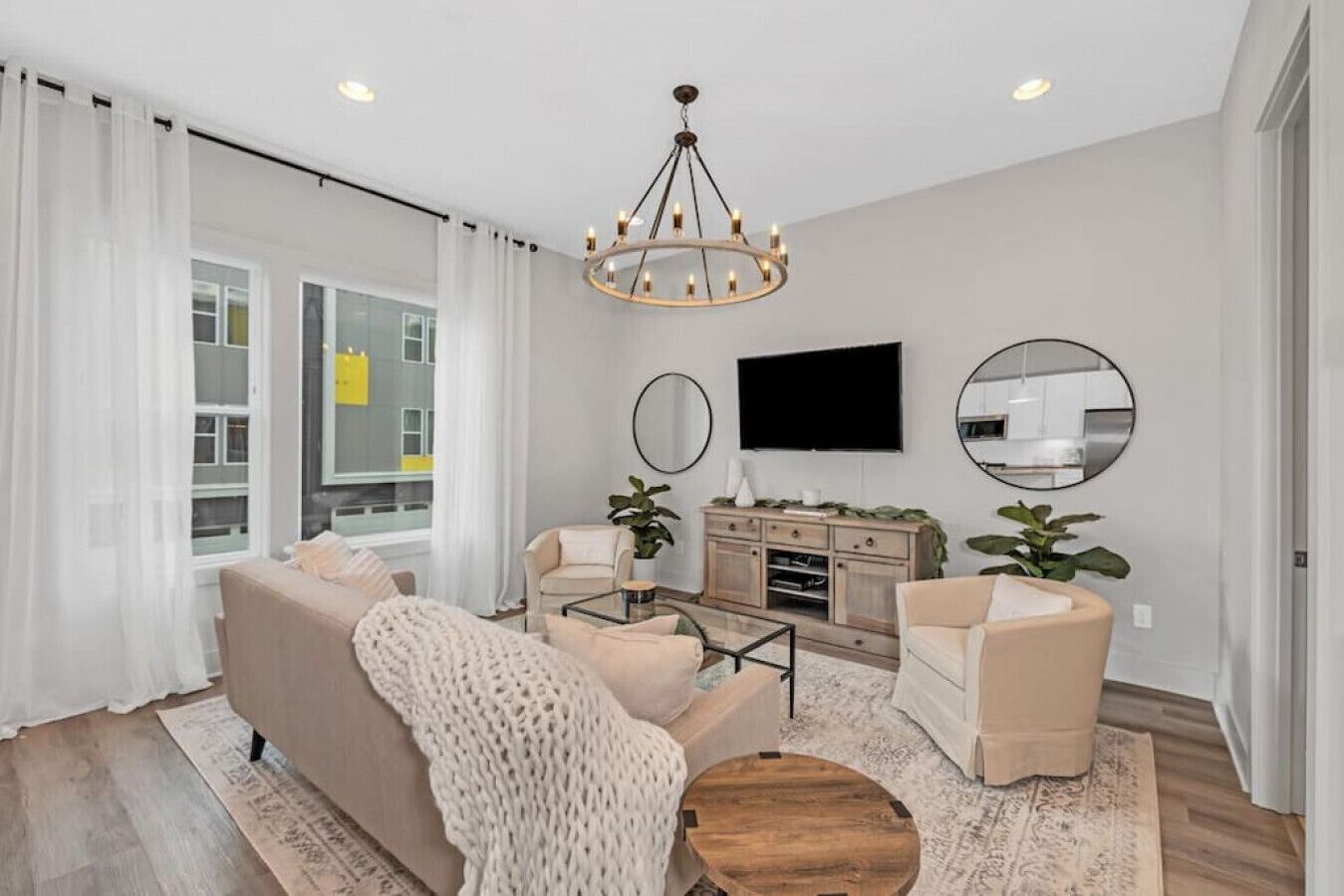 A modern living room with a sofa, armchairs, a coffee table, a TV, and a chandelier.