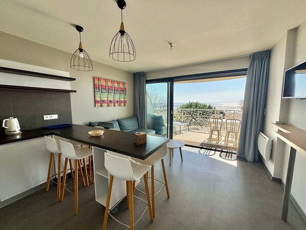 Una cocina moderna con comedor, sofá y balcón con mobiliario exterior.