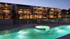 A hotel with a swimming pool, multiple balconies, and a well-lit exterior at dusk.