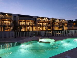 A hotel with a swimming pool, multiple balconies, and a well-lit exterior at dusk.