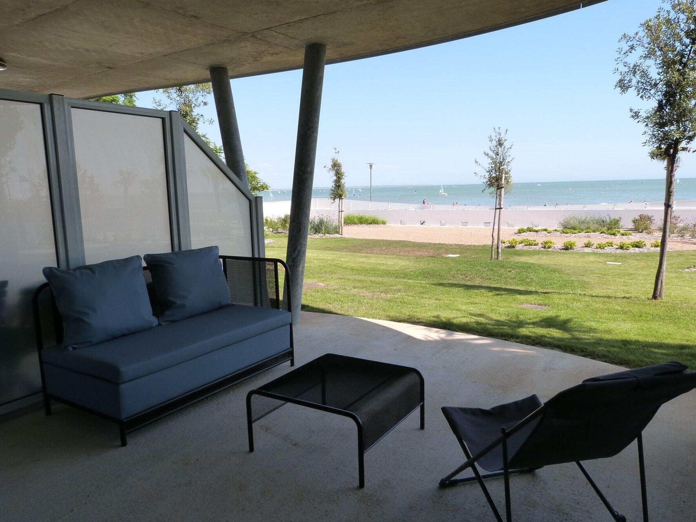 Een overdekt terras met een bank en stoelen, met uitzicht op een strand.