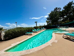 Une piscine avec plusieurs couloirs, entourée de chaises longues et de palmiers.