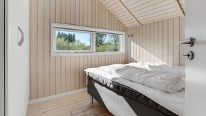Un dormitorio con una cama individual, paredes de madera, un tragaluz y vistas al exterior con vegetación.
