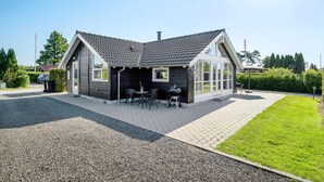 Una casa moderna con techo inclinado, un porche cubierto con muebles de exterior y un camino de entrada de grava.