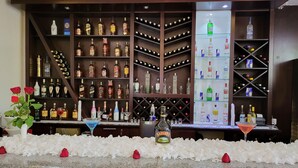 Zona de bar con estantes llenos de botellas de licores, vasos y un arreglo decorativo de flores blancas y rosas rojas.