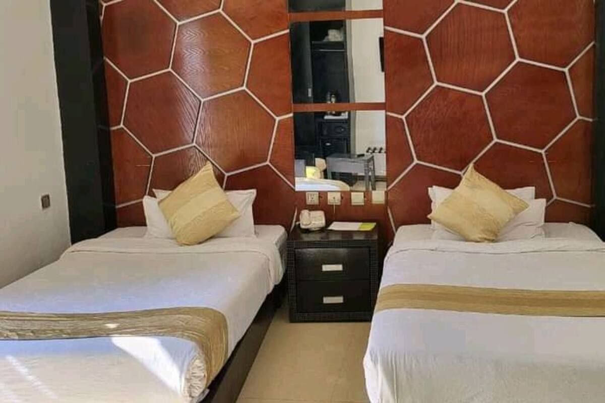A hotel room with two beds, a wooden headboard, a nightstand, and a mirror.