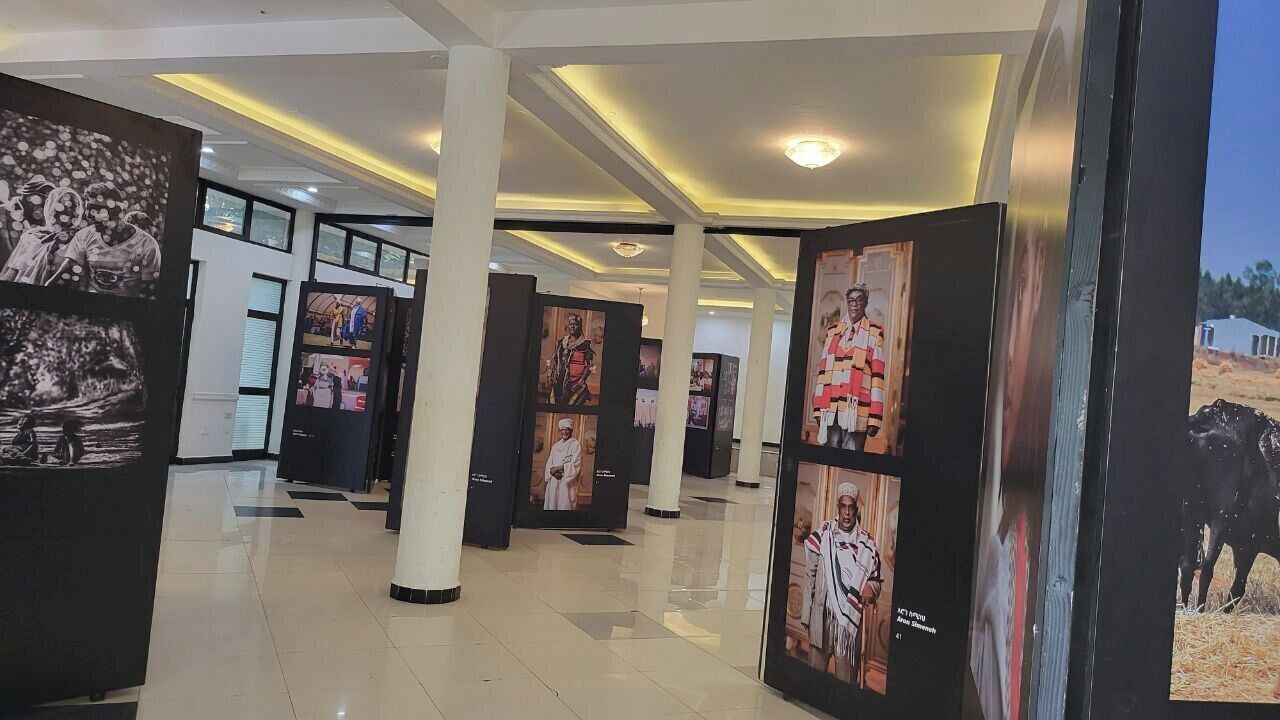 A corridor with framed photographs on display, white pillars, and a tiled floor.
