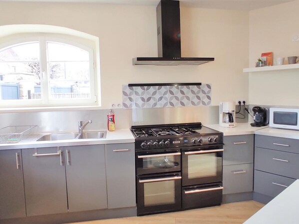 A modern kitchen with a gas stove, oven, and microwave. There is a window with a view of the outside, a sink, and a countertop with a coffee maker.
