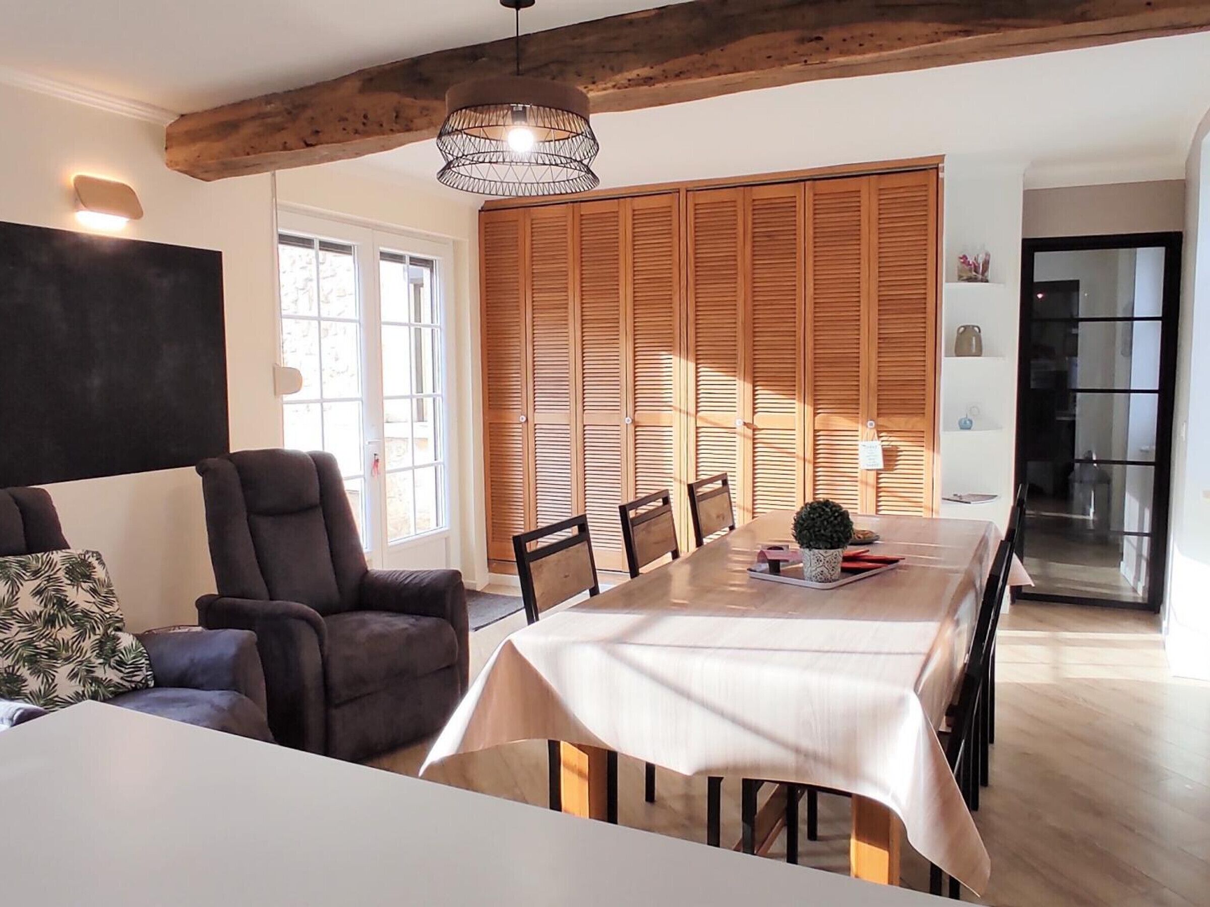 A dining area with a long table, chairs, a hanging light fixture, and a wooden wall with shutters.