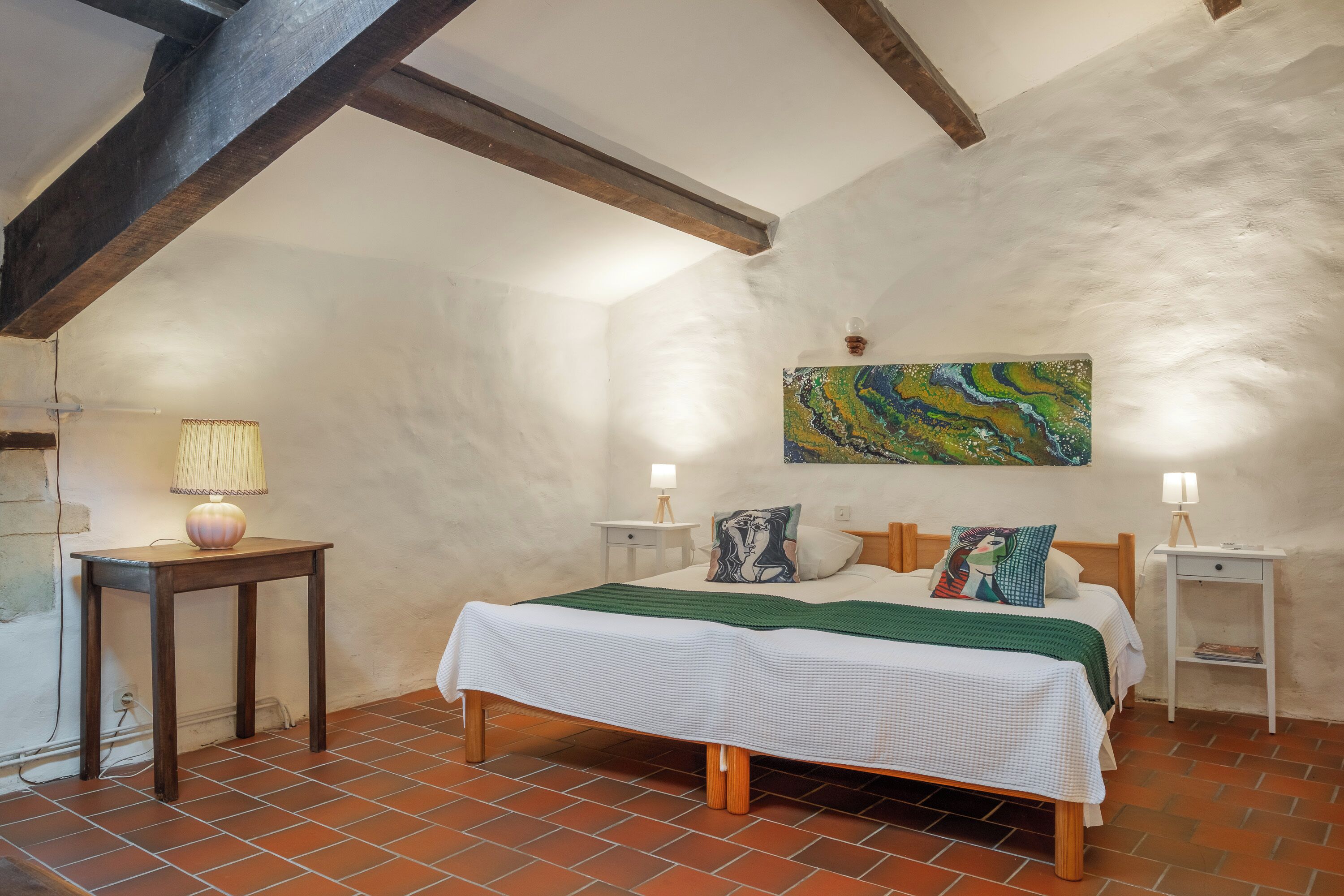 Een slaapkamer met een bed, twee nachtkastjes, een lamp, een schilderij en een betegelde vloer.