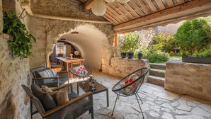 A stone-floored patio with wicker furniture, a wooden ceiling, and a view of a garden. - Large authentic house with swimming pool and tennis court, ideal for families and friends (LABASTIDE DE VIRAC)