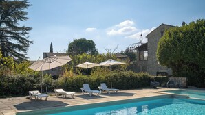 A swimming pool with lounge chairs and umbrellas, surrounded by greenery and a stone building. - Large authentic house with swimming pool and tennis court, ideal for families and friends (LABASTIDE DE VIRAC)