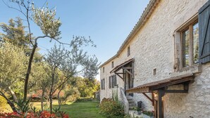 A stone building with a garden pathway leading to a wooden door. - Large authentic house with swimming pool and tennis court, ideal for families and friends (LABASTIDE DE VIRAC)