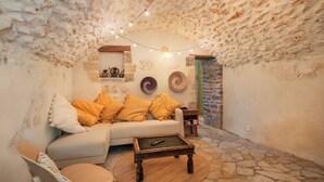 A cozy room with a stone wall, a sofa with yellow cushions, a wooden coffee table, and a small shelf with decorative items. - Large authentic house with swimming pool and tennis court, ideal for families and friends (LABASTIDE DE VIRAC)