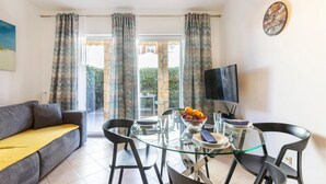 A living room with a sofa, a glass table with chairs, a bowl of fruit, a television, and a view of the outdoors through large windows. - 1 bedroom awesome apartment in Banjole (Banjole)