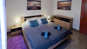 A neatly made bed with blue bedding and pillows, a wooden nightstand with a lamp, a wooden dresser, and two framed pictures on the wall. - 1 bedroom awesome apartment in Banjole (Banjole)