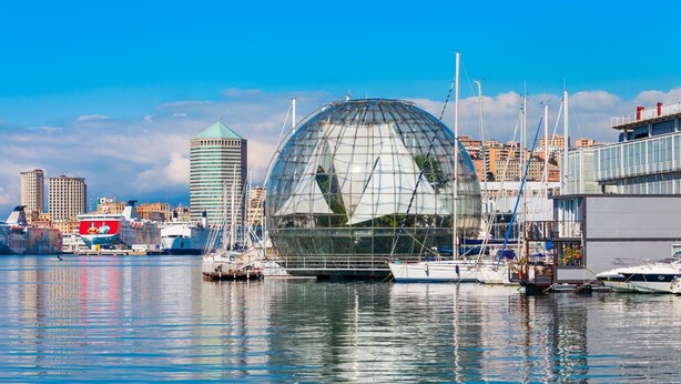 A waterfront view with a large glass dome structure, boats, and a city skyline in the background. - Modern and Cosy Apartment in Genoa, Italy (Genoa)