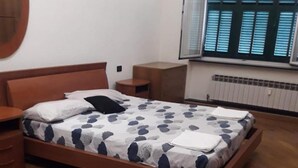 A bedroom with a wooden bed, a round mirror, a small bedside table, and a window with blinds. - Modern and Cosy Apartment in Genoa, Italy (Genoa)