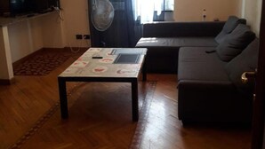 A living room with a sofa, a coffee table, a television, and a clock on the wall. - Modern and Cosy Apartment in Genoa, Italy (Genoa)