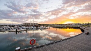 Een jachthaven met aangemeerde boten, een houten steiger en een zonsondergang op de achtergrond.