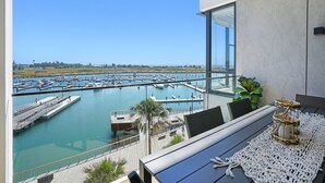 Een balkon met uitzicht op een jachthaven, een houten terras en een tafel met een geweven placemat.