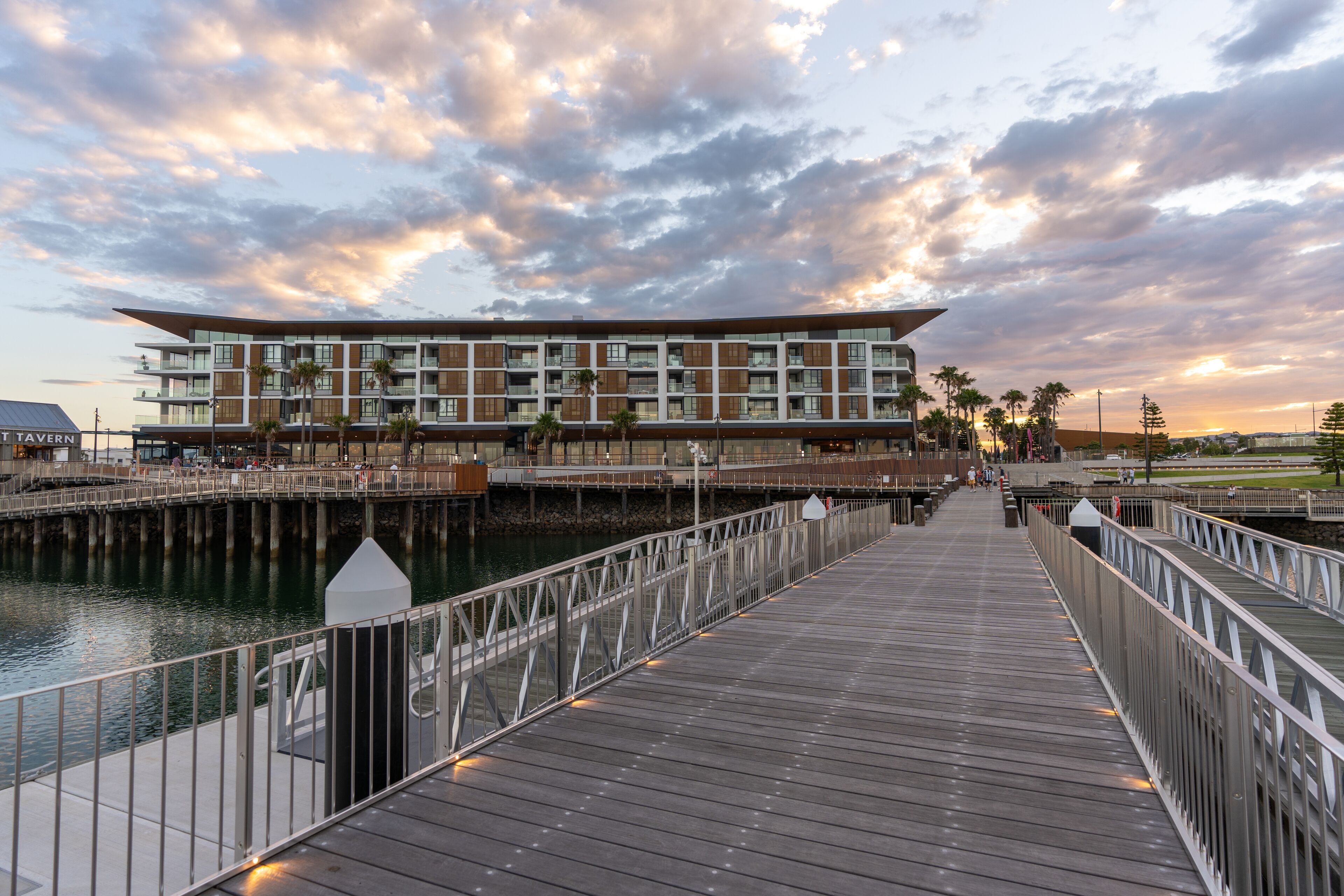 A waterfront promenade leading to a modern hotel with multiple balconies and a view of the water.