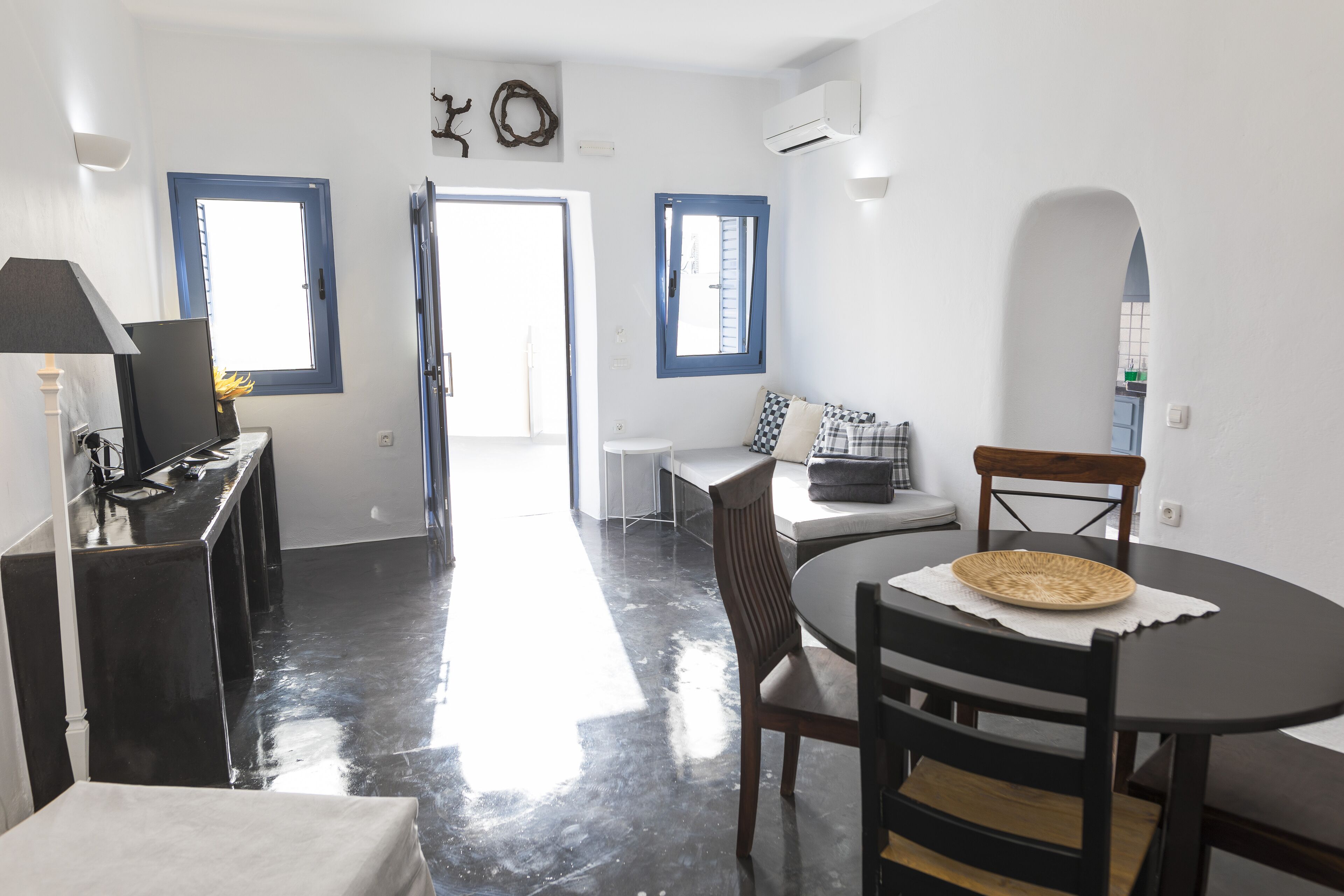 Una habitación moderna y luminosa con una mesa de comedor, sillas, una pequeña cocina y vistas a través de un ventanal abierto.