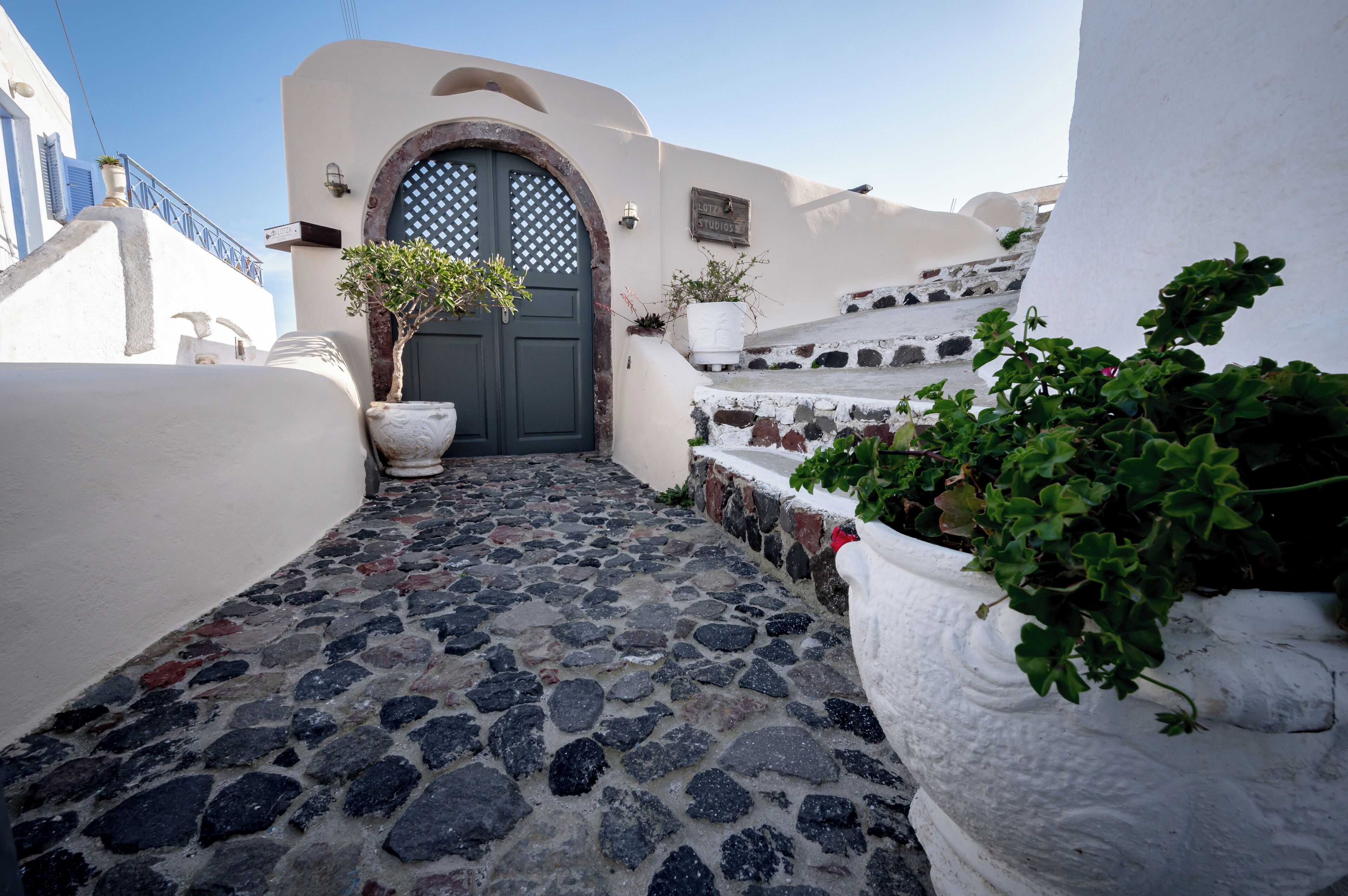 Un étroit sentier de pierre mène à un bâtiment doté d’une porte bleu foncé et de murs blancs.