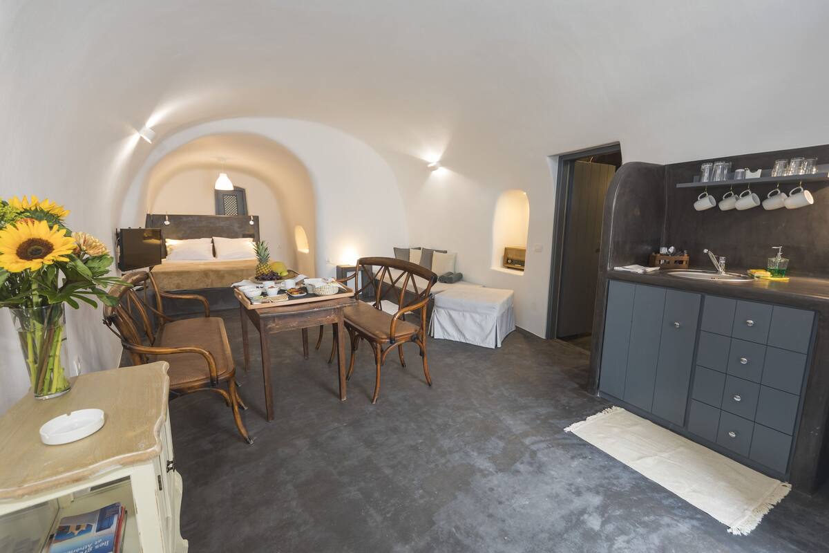 A compact kitchen with a dining area, a small table, and chairs. There is a sink, a countertop, and a shelf with cups.
