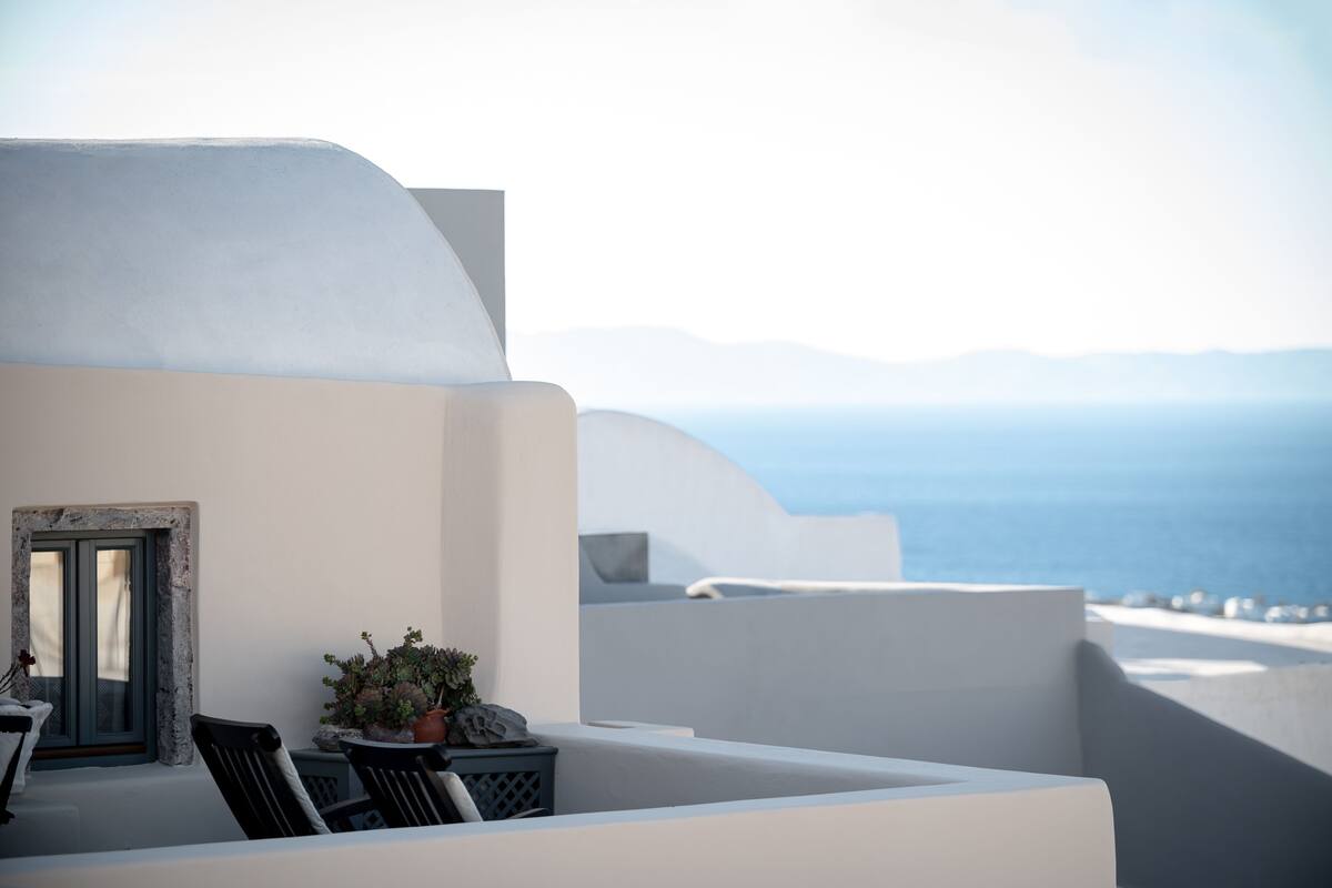 A white-walled room with a view of the sea and mountains.