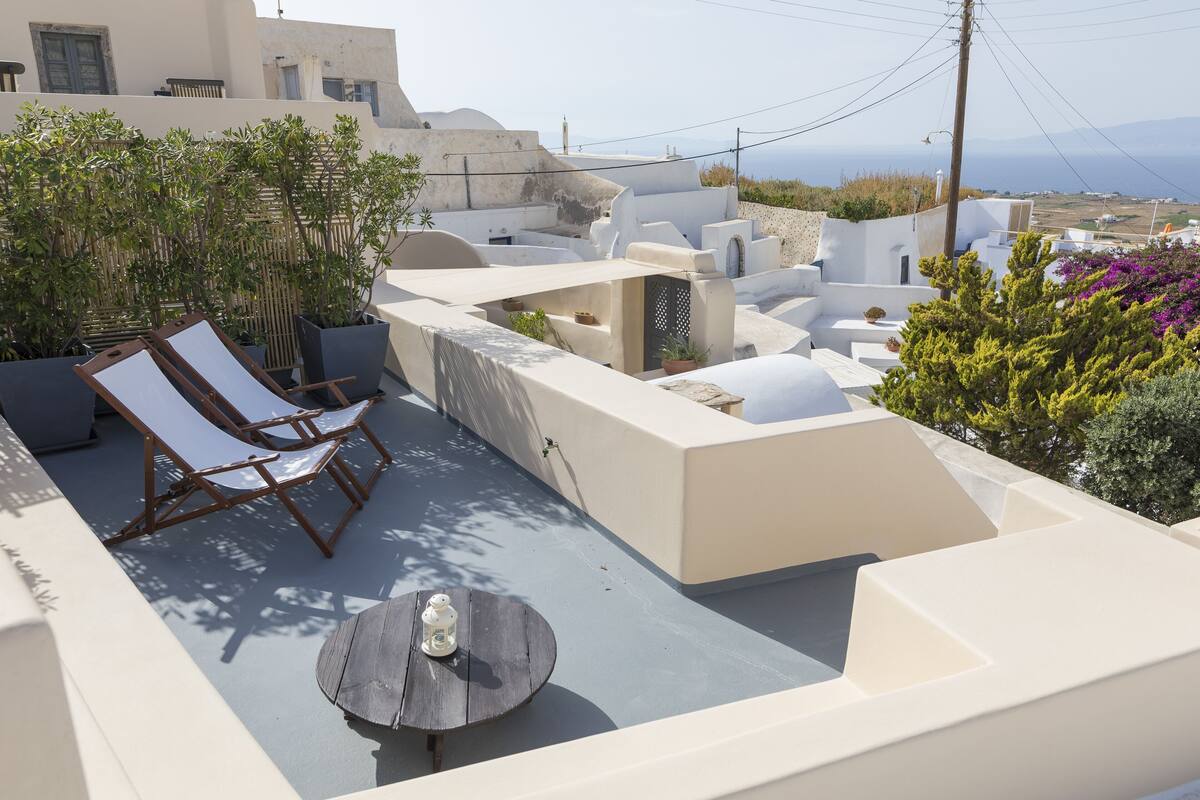 A rooftop terrace with white walls, a small table, and two lounge chairs.